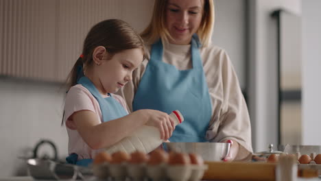 Kochen-Zu-Hause-Kleines-Mädchen-Hilft-Mutter-In-Der-Küche-Zugabe-Von-Milch-In-Teig-Oder-Omelett